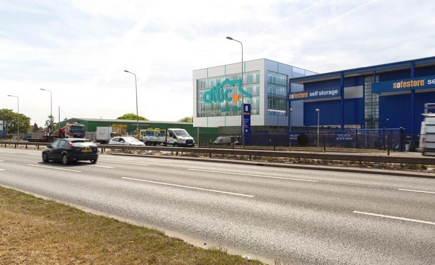 Car driving on a road near a blue and white building and the Attic Self Storage sign.