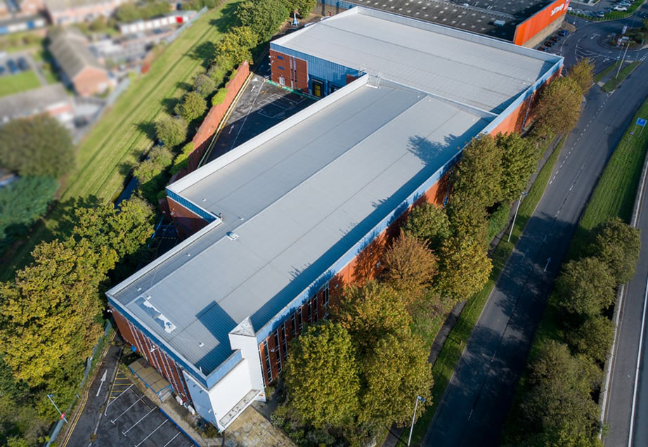 Aerial view of a large storage facility with a blue roof. Trees surround the building.